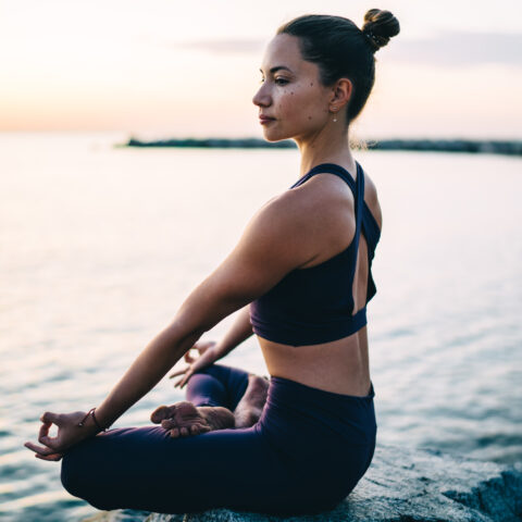 Muscular woman enjoying yoga during morning sea breathing training body shape in asana